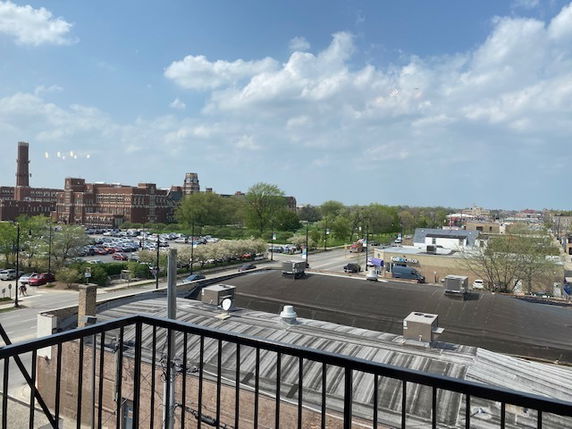 Panoramic view of surrounding area from a balcony, showing buildings and parking areas.