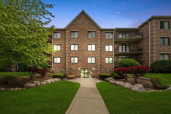 Front view of a multi-story brick building with balconies and landscaped entrance.