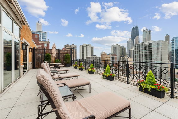 Rooftop area with lounge chairs and planters offering a view of city skyscrapers.