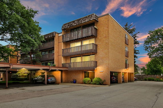 Front view of a multi-story brick apartment building with balconies and carport.