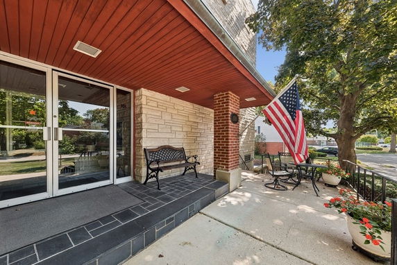 Front view of a building entrance with a glass door, bench, and American flag.