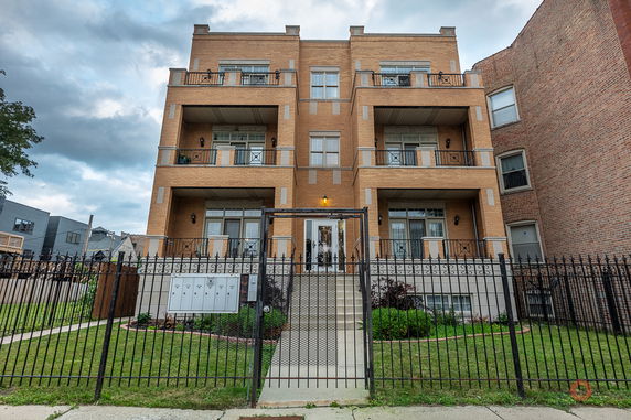 Front view of a multi-story brick residential building with balconies and a gated entrance.