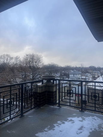 Panoramic view from a balcony showing a railing with geometric designs and a cloudy sky.