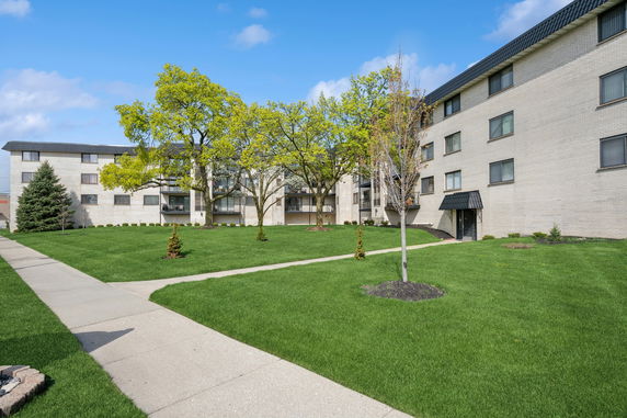 Front view of a multi-story apartment building with a well-maintained lawn and trees.