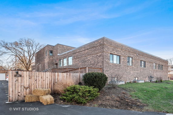 Front view of a brick two-story building with a wooden fence and driveway.
