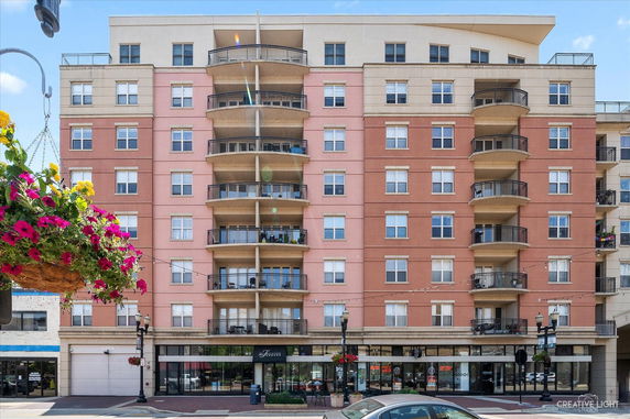 Front view of a multi-story building with balconies and shops on the ground floor.