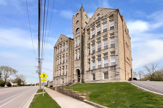 Front view of a multi-story stone building with arched entrance and corner tower.