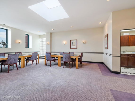 Indoor area with tables and chairs, likely used for meetings or recreation, featuring a skylight and adjoining kitchenette.