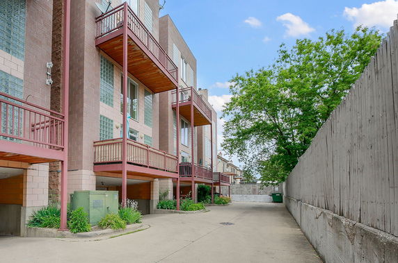 Front view of a multi-story building with balconies and a fenced driveway.