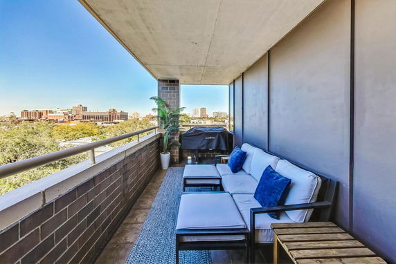 View of an outdoor balcony with seating and a cityscape in the background.