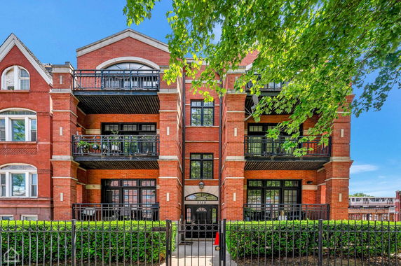 Front view of a multi-story brick apartment building with balconies and a gated entrance.
