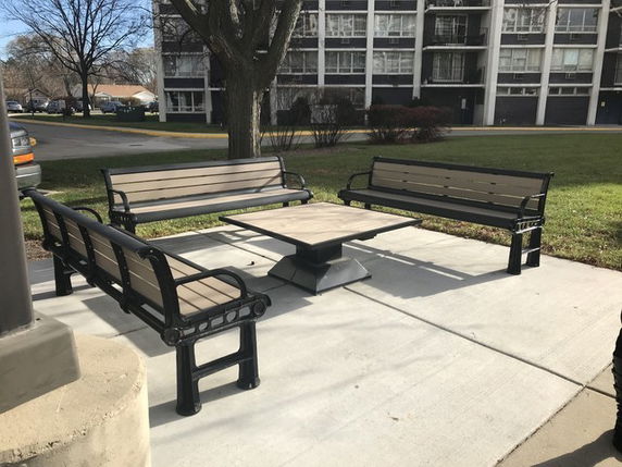 Outdoor seating area with benches and a table in front of a multi-story building.