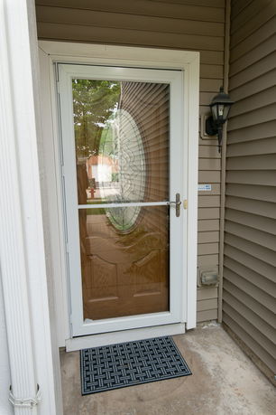 Front door of a house with a glass storm door and brown siding.