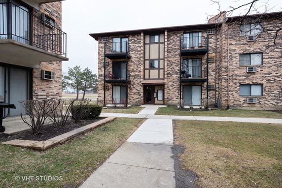 Front view of a multi-story apartment building with balconies and brick exterior.