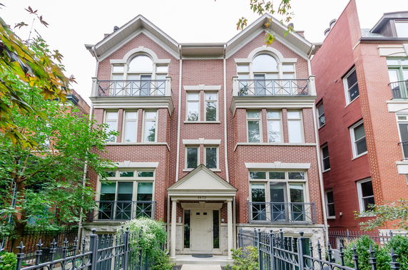 Front view of a four-story brick townhouse with a gabled roof and balconies.