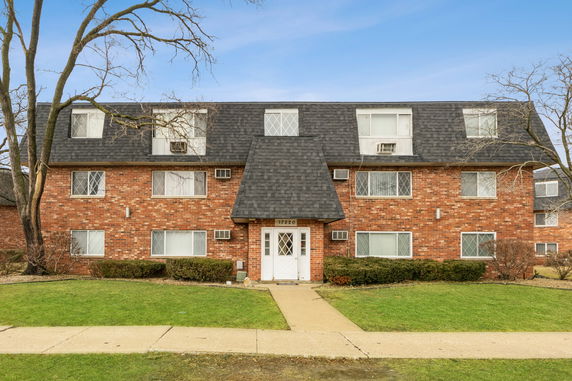 Front view of a multi-story brick building with a dark shingled roof and multiple windows.