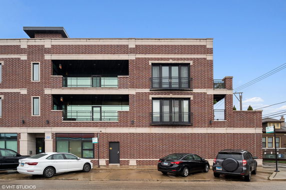 Front view of a multi-story brick building with balconies and parking space.