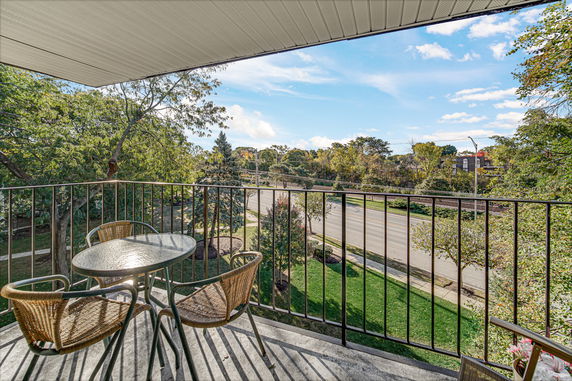 Balcony view overlooking a road and lush green trees under a clear blue sky.