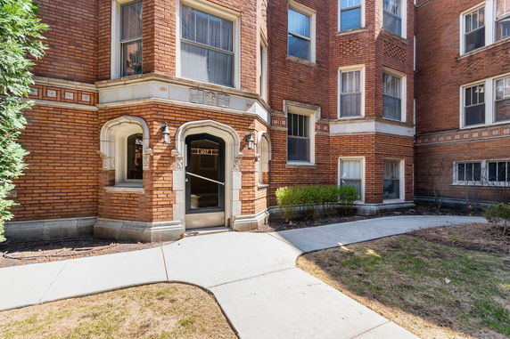 Front view of a multi-story brick apartment building with decorative arches at the entrance.