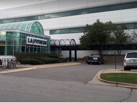 Front view of a fitness center with a glass-covered entrance and adjacent parking area.