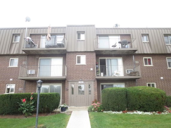 Front view of a three-story brick apartment building with balconies.