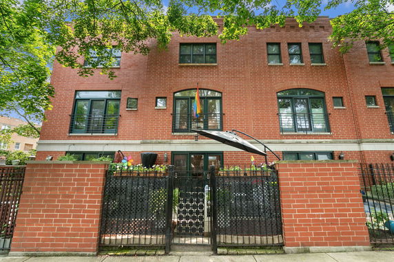 Front view of a multi-story brick building with large windows and a fenced entrance.