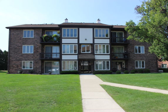 Front view of a three-story brick apartment building with balconies.