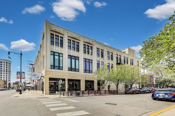 Front view of a three-story building with large windows and a sidewalk patio.