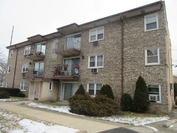 Front view of a three-story brick apartment building with balconies.