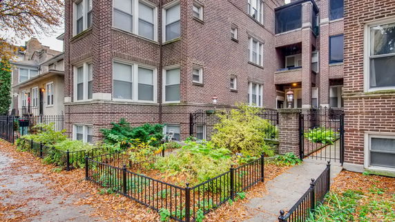 Front view of a multi-story brick apartment building with fenced garden.