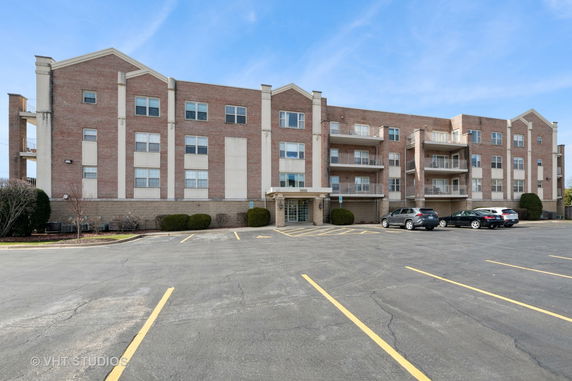 Front view of a multi-story brick apartment building with balconies and parking area.