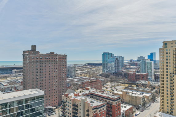 Panoramic view of city buildings and distant body of water under a cloudy sky.