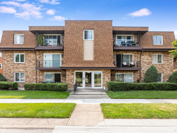 Front view of a three-story brick apartment building with balconies.