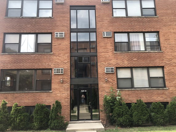 Front view of a multi-story brick apartment building with several windows and a central entrance.