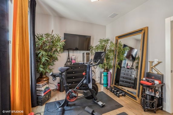 Home gym area with exercise bike, large mirror, TV, and plants.