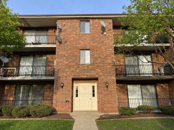 Front view of a three-story brick apartment building with balconies and satellite dishes.