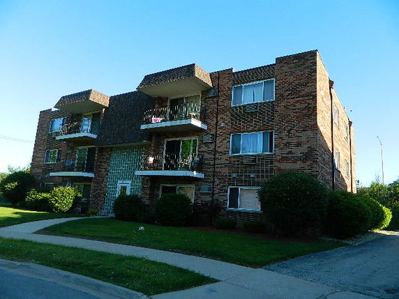 Front view of a three-story brick apartment building with balconies.