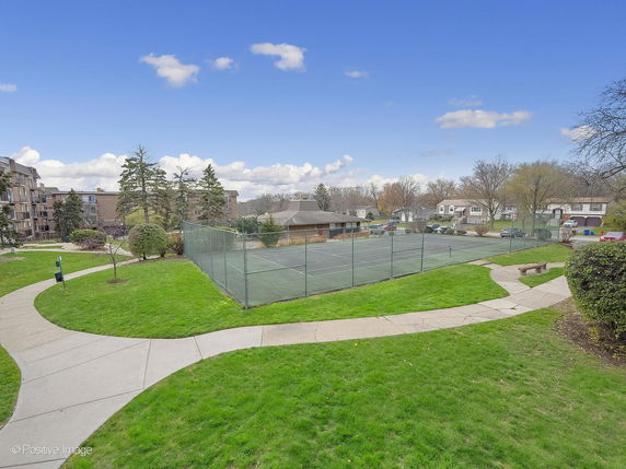 View of a tennis court surrounded by pathways and buildings.