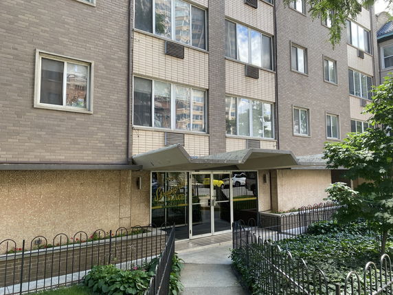 Front view of a multi-story residential building with entrance and large windows.