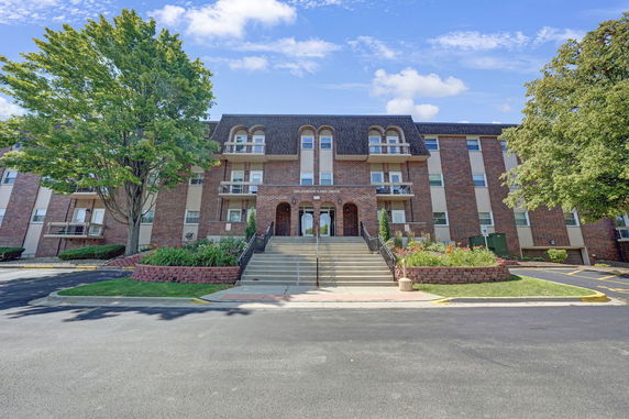 Front view of a multi-story brick building with balconies and an entrance staircase.