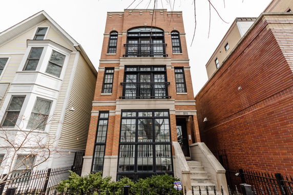 Front view of a multi-story brick building with large windows and a staircase leading to the entrance.