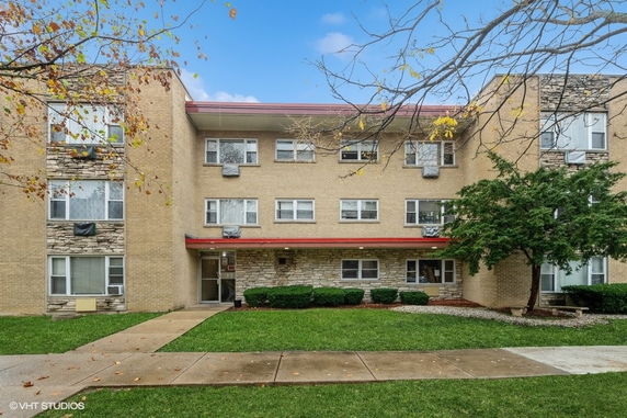 Front view of a three-story apartment building with beige brick exterior.