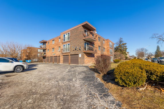 Front view of a three-story brick apartment building with balconies and garage spaces.