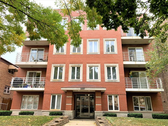 Front view of a multi-story brick apartment building with balconies.