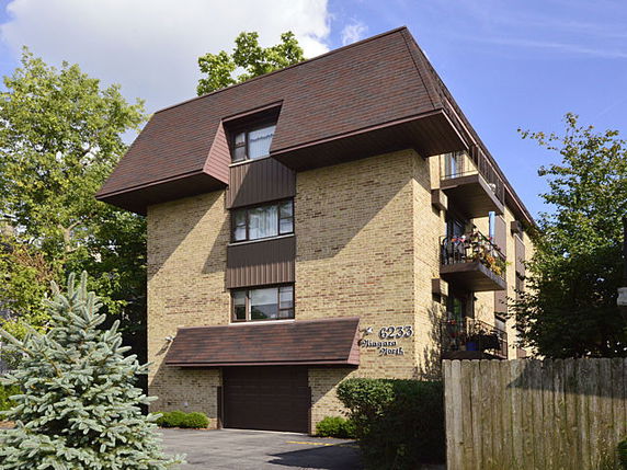 Front view of a three-story building with a slanted roof and brick facade.