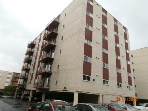 Front view of a multi-story apartment building with balconies and parking area below.
