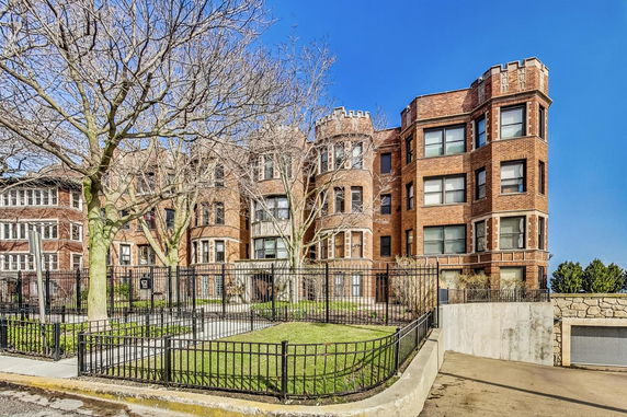 Front view of a multi-story brick apartment building with bay windows and a gated entrance.