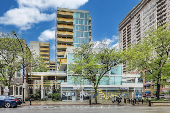 Front view of a multi-story residential and commercial building with glass and yellow accents.