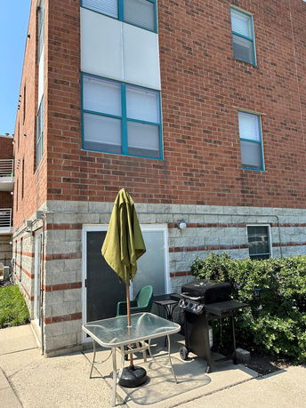 Front view of a brick apartment building with a patio set and grill outside.