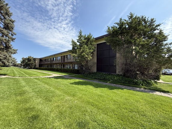 Front view of a two-story building with large windows and a flat roof surrounded by greenery.